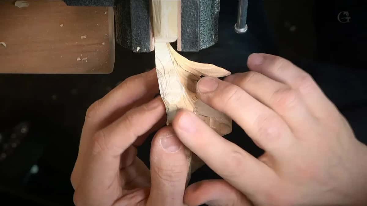 Cupped hands hold a narrow carved leaf, the fingers wider than the wood between them.