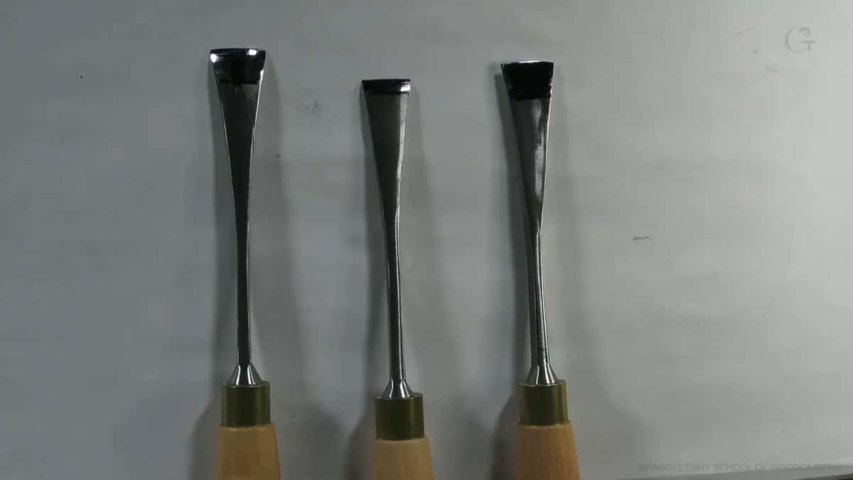 Three carving gouges of different blade widths stand upright, showing polished steel and brass ferrules.