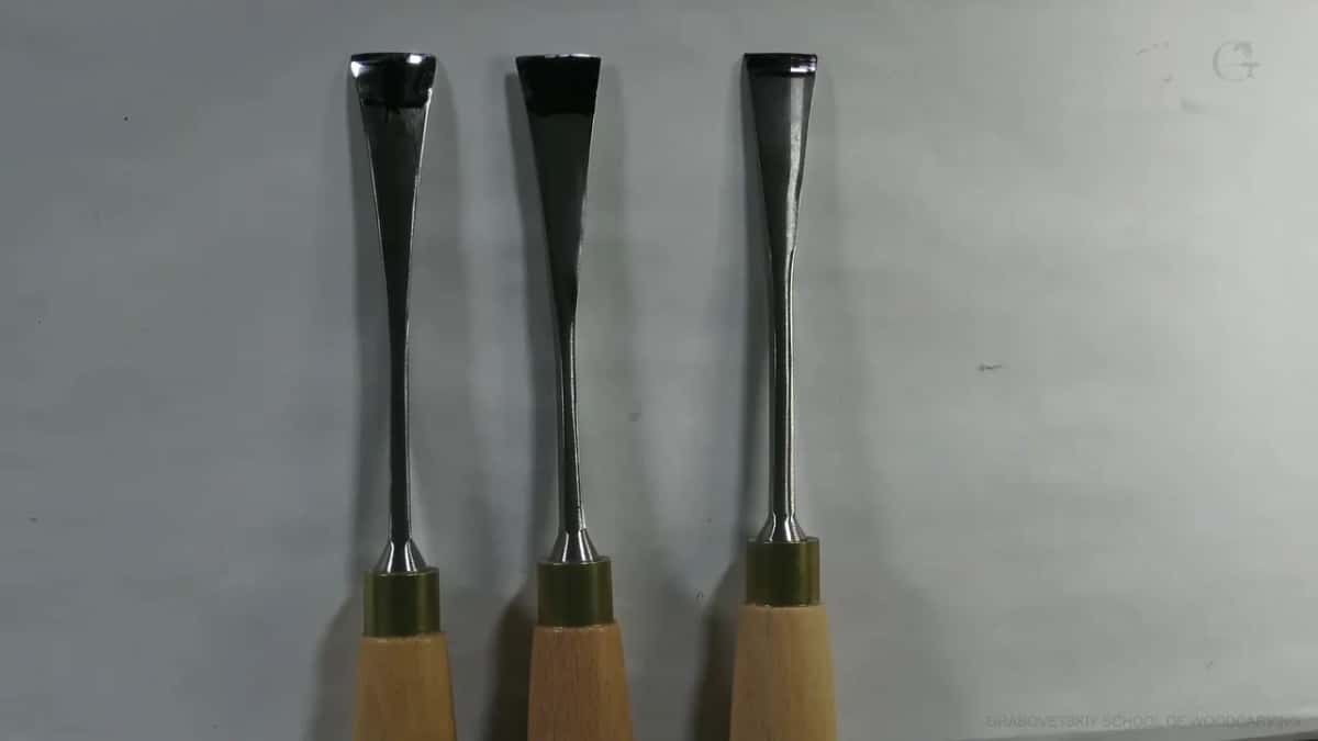 Three carving gouges lie side by side, showing their long thin metal necks and beveled tips.