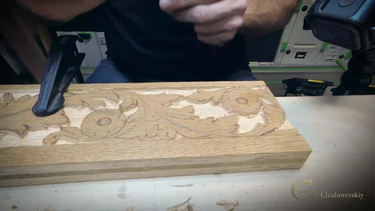 A tan board with strong straight grain bands, carved along its face with scrolls and two rosettes.