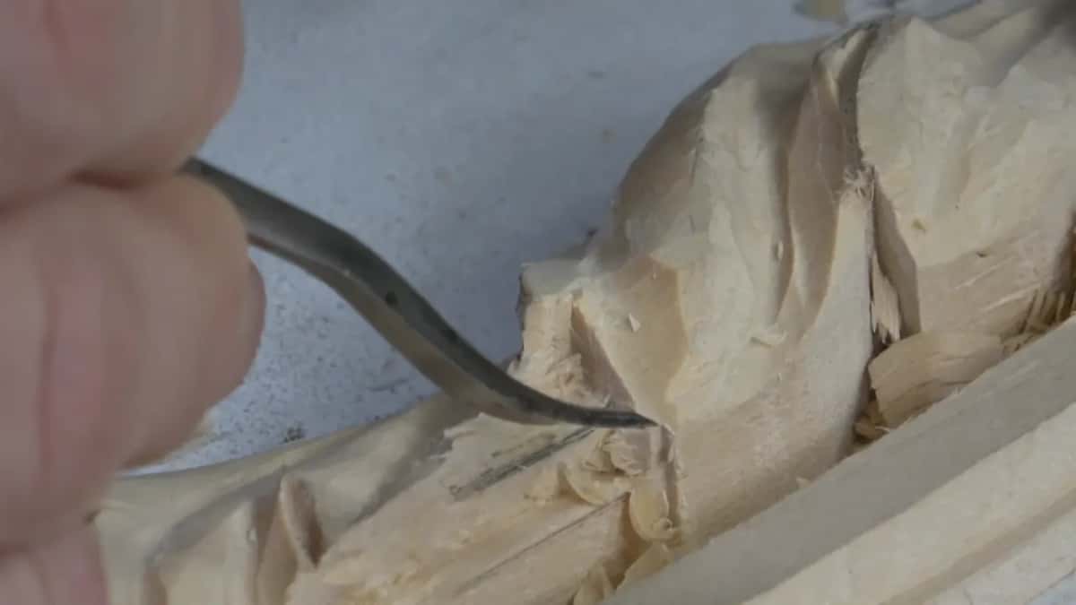 Extreme close view of a bent tool sliding into the shadow pocket beneath a pale carved leaf.