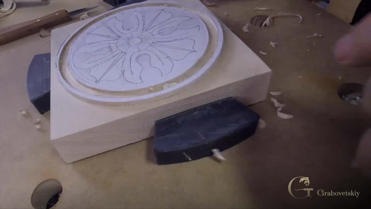 A thick pale block clamped on the bench, the round rosette drawing outlined and the ring already sunk.