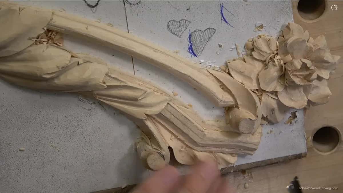 A pale carved scroll runs into a cluster of open flowers, each petal carved free of the one behind.