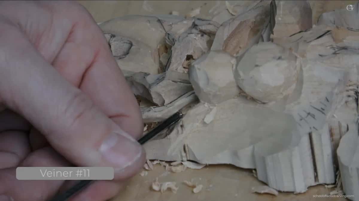 A narrow gouge shapes round bead forms on a roughed-out wood carving, chips scattered below.