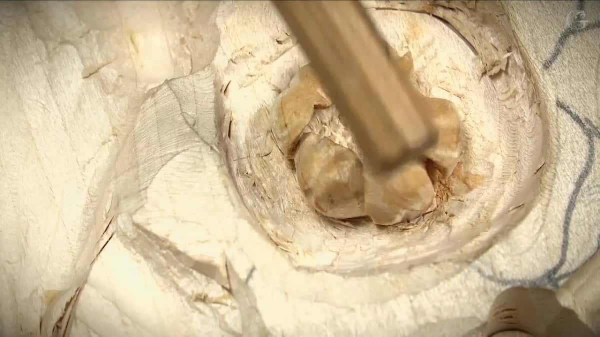 Looking straight down into a deep round hollow carved in pale wood, a tool handle rests inside it.