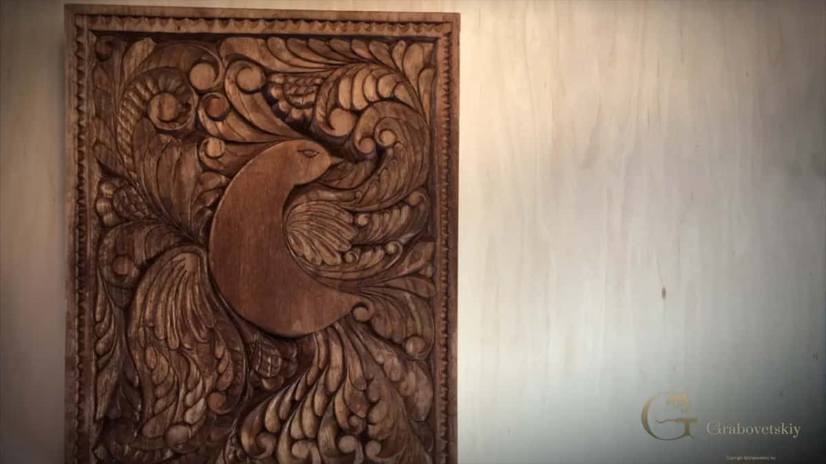 The finished panel leans in soft light, brown and carved deep, a bird resting among curling leaves.