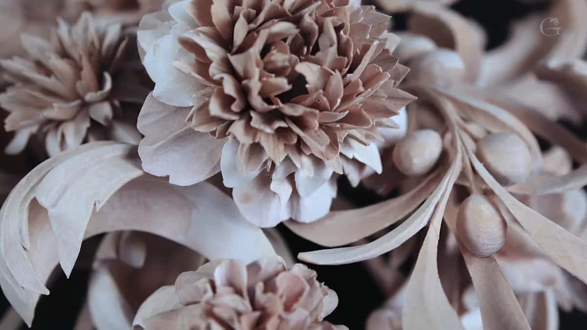 Carved flowers in pale wood crowd together, petals layered deep, leaves and buds curling into shadow.