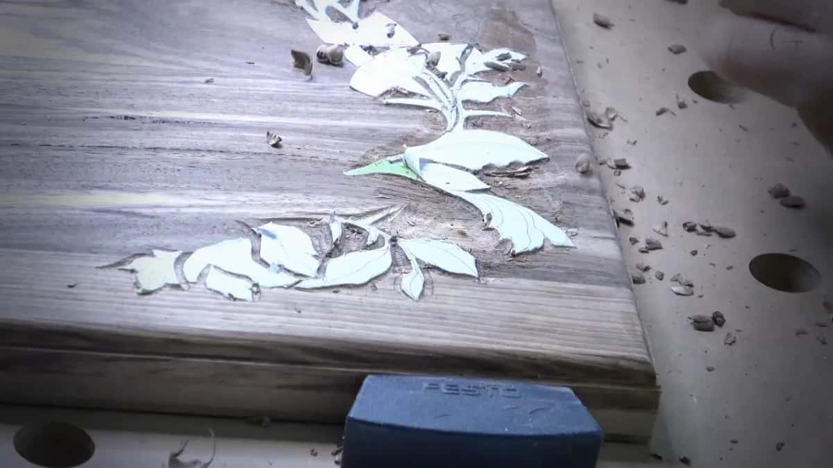 A pale printed leaf pattern sits on a dark brown board, brown chips scattered over the wood and bench.