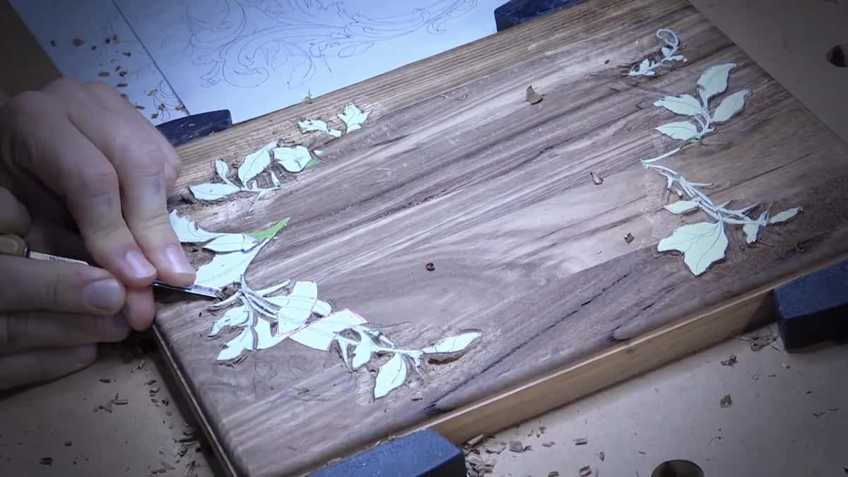 A small tool follows the pale leaves on a clamped dark board while loose chips lie all around it.