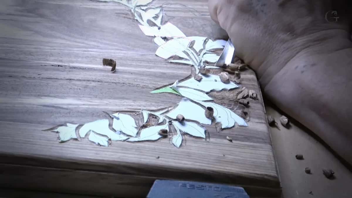 A blade works beside the pattern on a dark board and a small heap of brown chips builds along its edge.