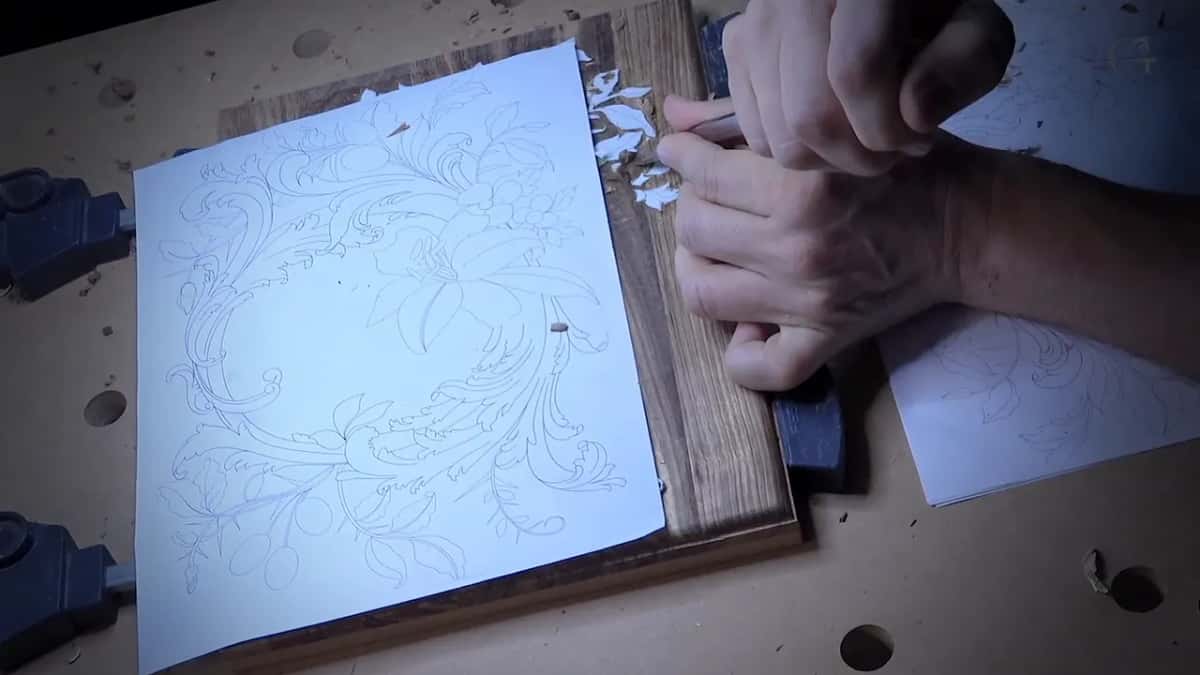 A big pencil drawing lies over a dark board, hands working at the right where the paper is folded back.