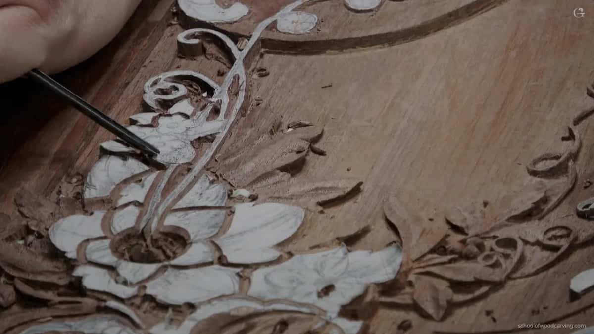A thin dark tool reaches into a white flower on a brown board, the smooth field of wood open to the right.