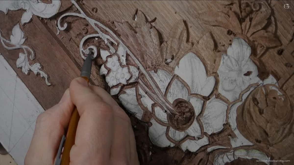 Held low in the fingers, an orange handled tool works a large white flower on a brown board.