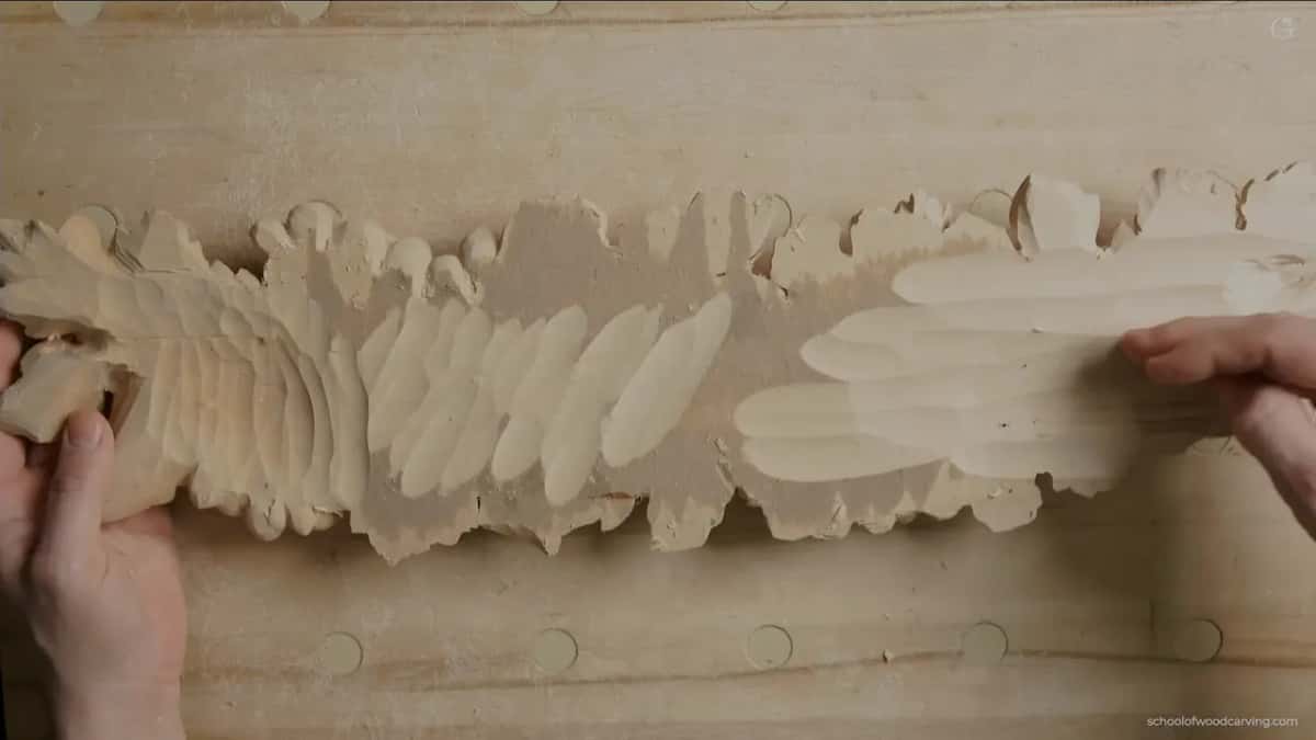 A long relief molding shows a row of carved wavy ridges, held steady at both ends while the surface is refined.