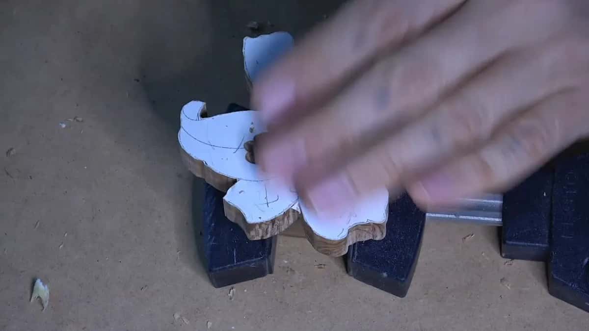 Held in a bench vise, a small wood blank carries a paper pattern glued to its top face.