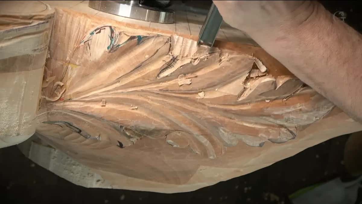 Forearm across the block while a gouge works the upper edge of the leaf, beside the clamp