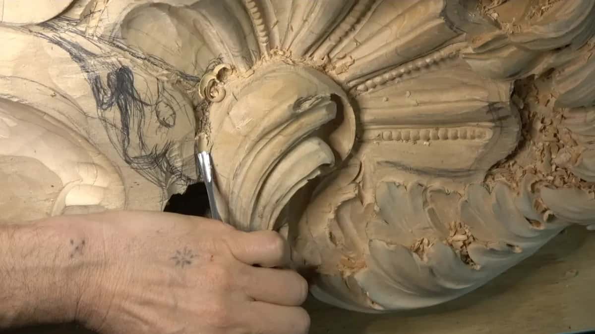 Fingers hold a gouge against the rim of the scroll, with the sketch to its left.