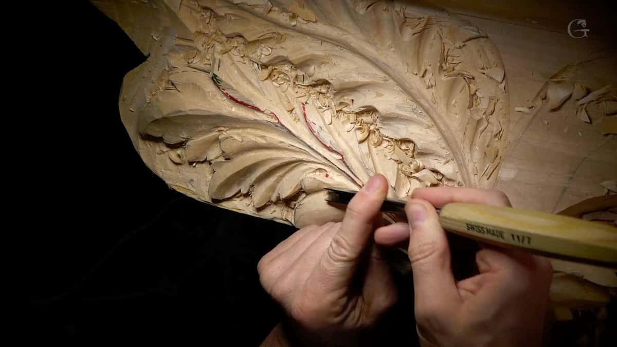 Two hands holding a Swiss gouge low against an acanthus leaf, red and green pencil in the grooves.