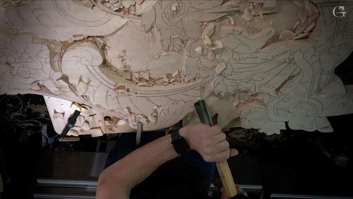 A close-up shot of a wood carving in progress shows intricate designs taking shape. The craftsman hammers a chisel into the wood surface, surrounded by shavings and curls from the work. This image captures the essence of wood carving lessons, showcasing skill and artistry that come with dedicated practice in wood carving classes.