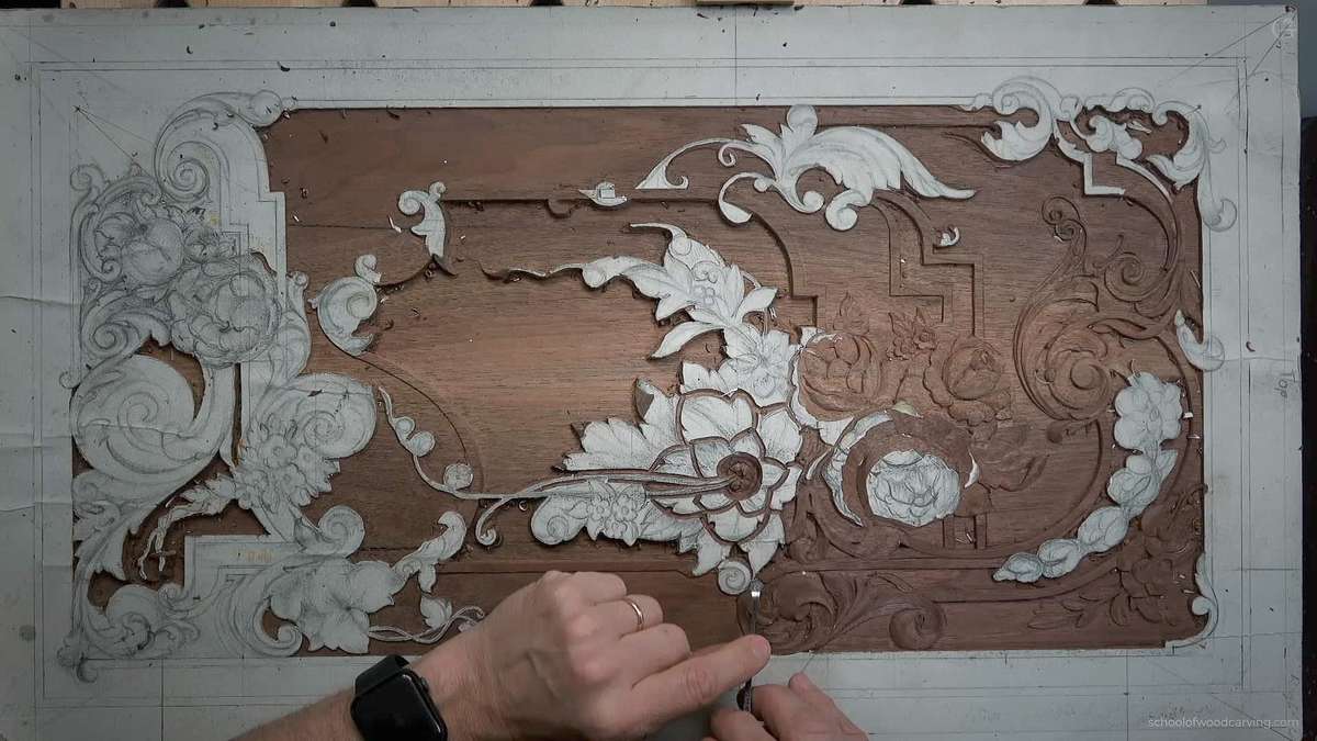 Alt text: A close-up of a wood carving project in progress, showcasing detailed floral designs etched into the surface. The artist's hands are seen delicately working, tools like chisels nearby, illustrating the intricate process of wood carving. Ideal for those interested in wood carving classes and lessons.