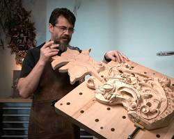 A person demonstrating wood carving techniques in a workshop, showcasing a detailed carved piece on a workbench. This image highlights the artistry involved in wood carving classes and lessons.