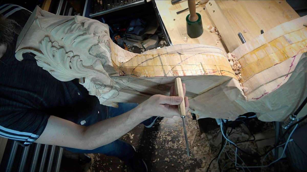 A person carving intricate designs into a piece of wood while holding a compass. Wood shavings and carving tools for beginners are scattered around, inspired by woodcarving tutorials online.
