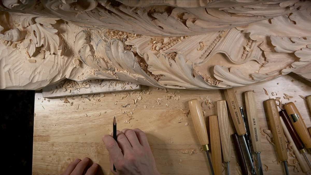 A pair of hands working on intricate wood carving, with woodworking tools and wood shavings spread out on a wooden surface, reminiscent of the techniques found in woodcarving tutorials online.