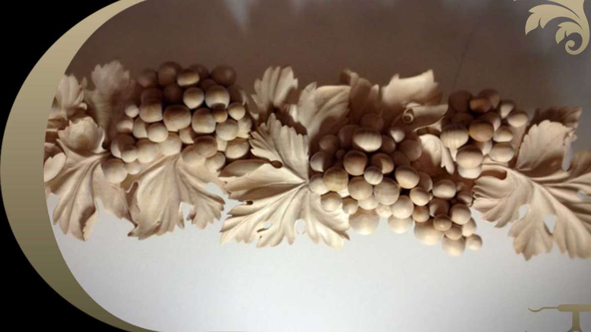 A detailed wood carving depicts a cluster of grapes with leaves, positioned under soft lighting, casting gentle shadows. It's a fine example of what can be achieved by taking woodcarving classes for adults.