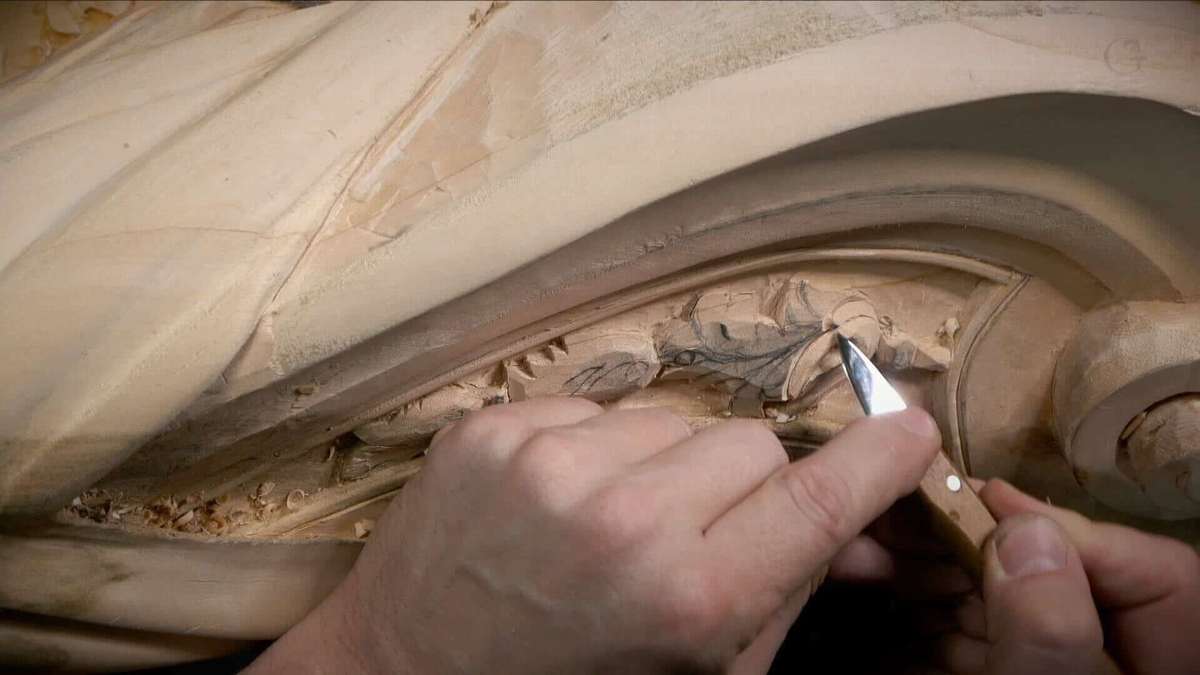 A person is carving a detailed design in wood using a small carving knife. Close-up of hands working on the piece, highlighting the texture of the wood and the careful attention paid to each cut. Ideal for those looking for wood carving classes or wood carving lessons.