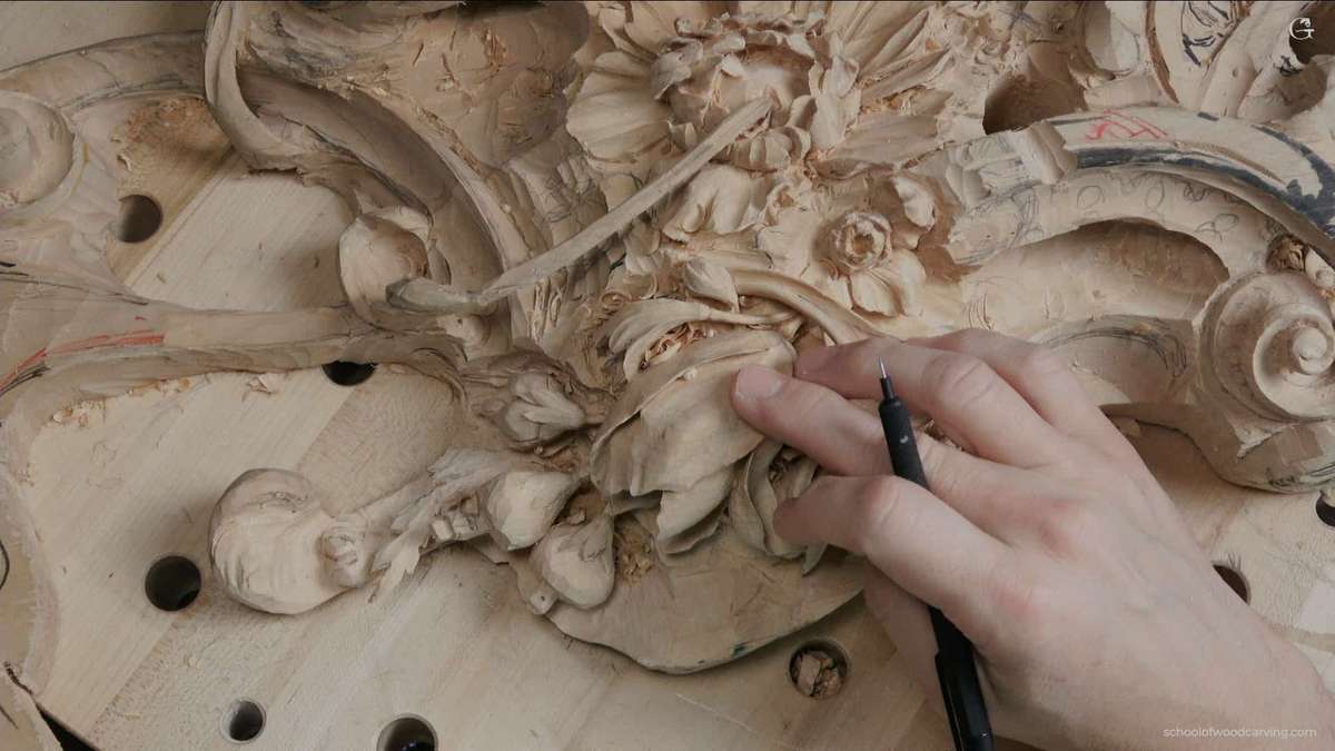 Close-up view of a hand holding a pencil, pointing at a meticulously crafted tulip flower featured on a Grinling Gibbons woodcarving. The woodcarving masterpiece showcases the detailed craftsmanship of woodcarving. Grinling Gibbons' woodcarving techniques are evident in the intricate design. The pencil underscores the precision involved in woodcarving. Tulip flower, a highlight of the woodcarving, depicts the realistic approach of Grinling Gibbons' woodcarving style. The woodcarving composition presents a harmonious blend of nature and art. An unmissable piece of woodcarving art demonstrating the timeless beauty of Grinling Gibbons' woodcarving legacy. The woodcarving reveals the artist's meticulous attention to detail. This woodcarving is a testament to the skills required in creating such intricate works of art. Explore the depth and texture of this stunning example of Grinling Gibbons' woodcarving prowess.