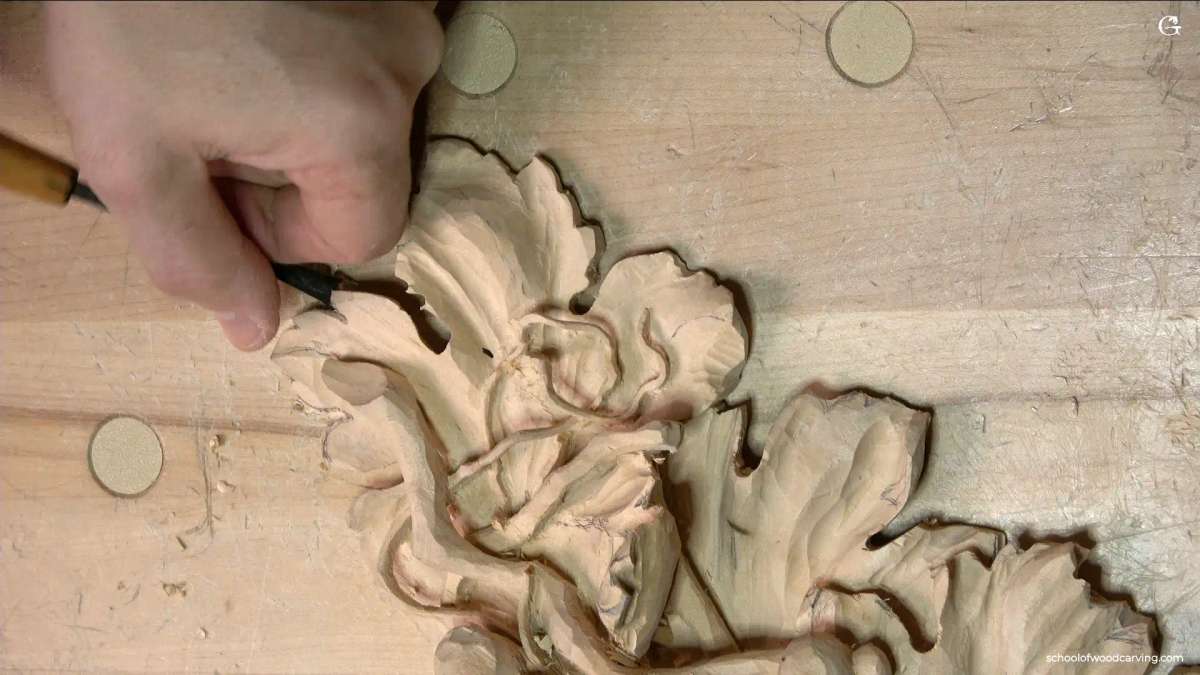 WOODCARVING LESSONS: Woodcarver Grabovetskiy carves a floral pattern in light wood, showing textured leaves and petals for woodcarving tutorials. - Wood Carving tutorials