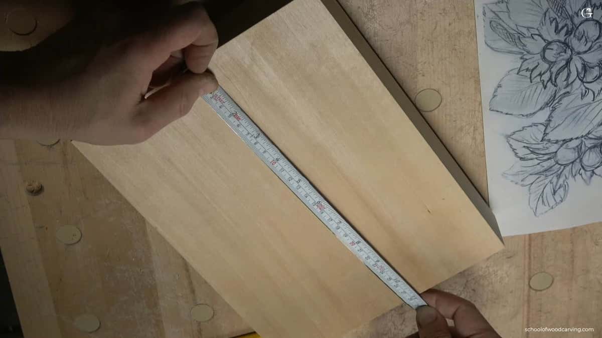 Reading the board, not the calendar One hand holds a steel tape laid across a plain pale carving board, a pencilled hazelnut drawing right beside it