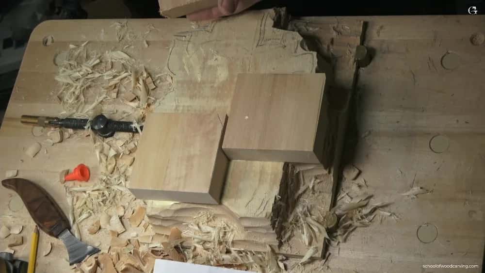 The size a kitchen can manage Three plain square blocks of pale wood resting on a shaving covered bench, a carving knife and glue nozzle nearby