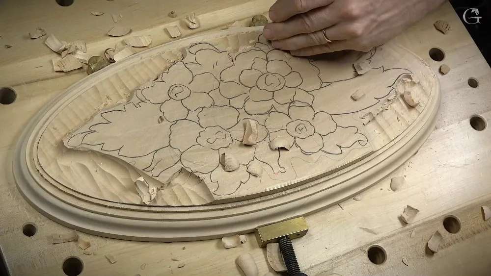 Carver's hands shape a floral relief design in light wood using traditional hand tools