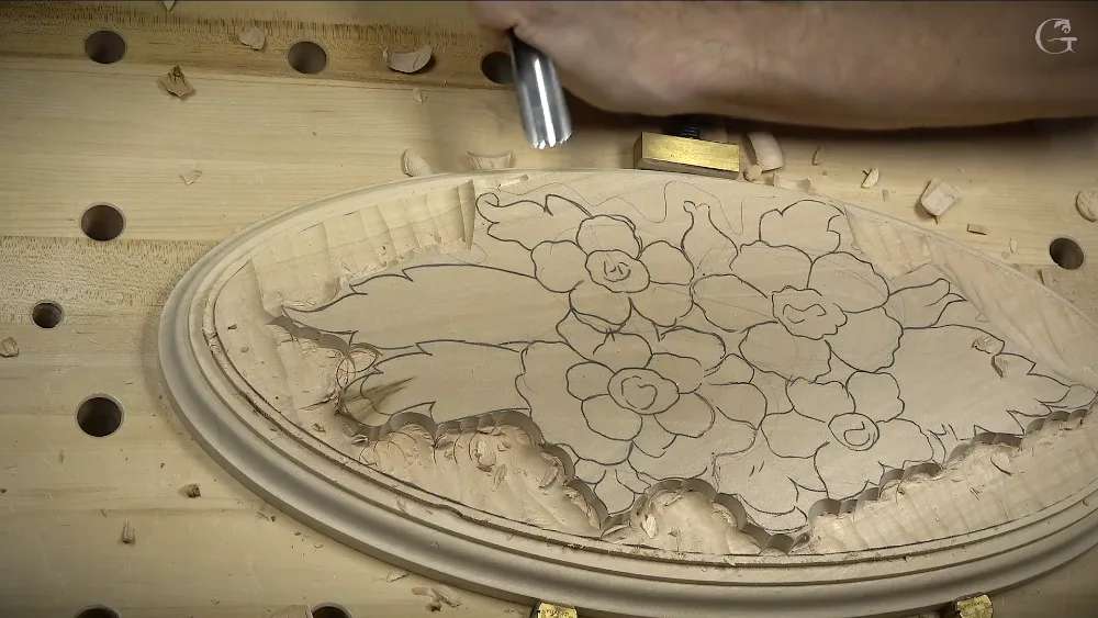 Carved wood relief showing flowers and leaves on an oval panel with tool marks visible