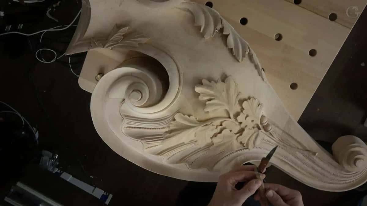 Large console bracket with a rolled volute and acanthus leaves lies on the bench while a knife cleans the beading along its lower edge