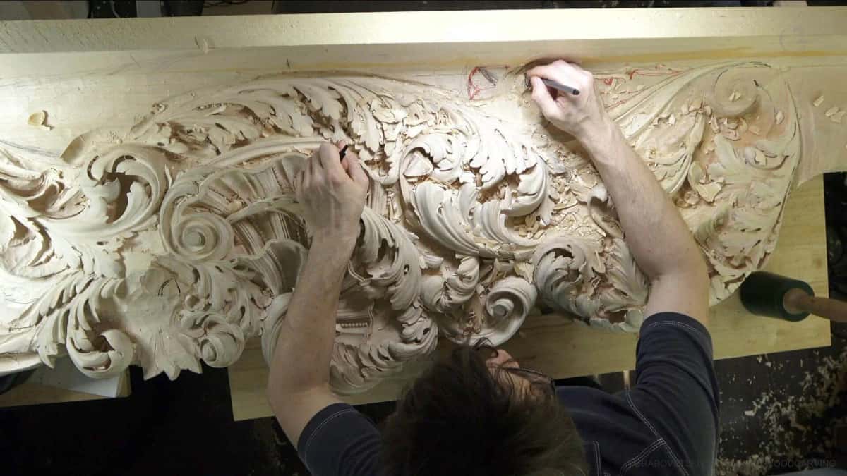 Dense baroque acanthus scroll under the gouge along a long panel, red layout marks still on the wood