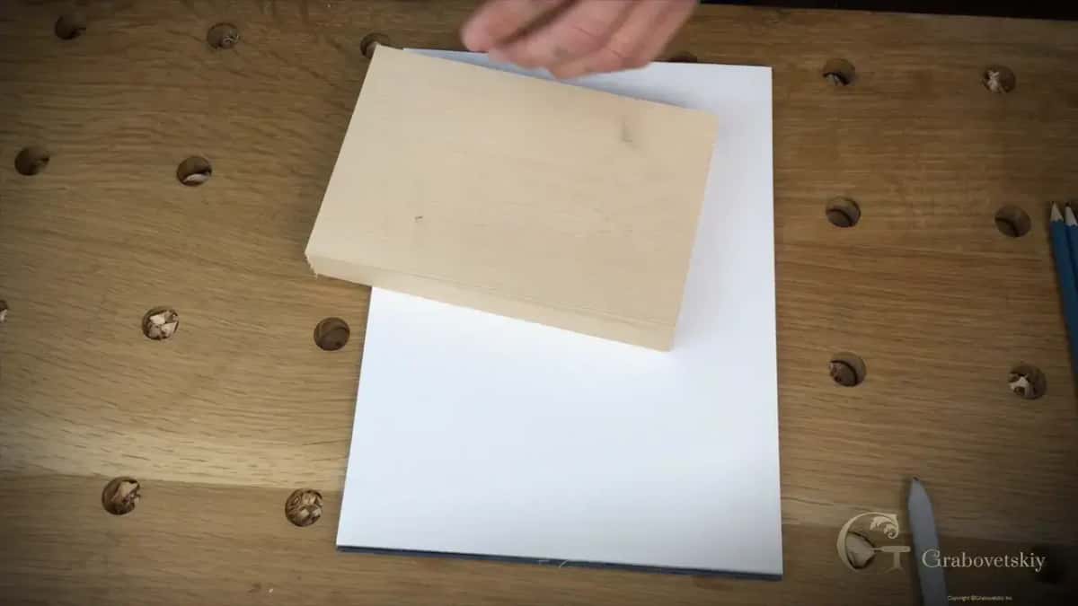 Basswood block resting on a sheet of printer paper, ready to be glued down for the sandwich mount, the bench dog holes ranged around it