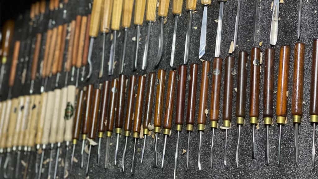 A row of carving gouges in a roll, handles turned from different woods, each blade ground to its own sweep