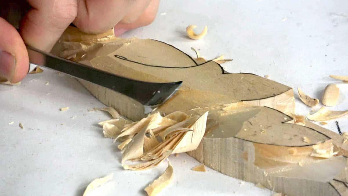 A wide gouge lifting long shavings as the background drops away around the leaf