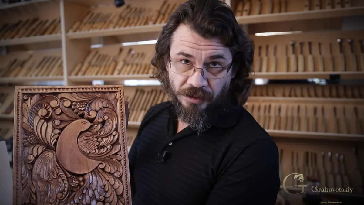 Alexander holding up the finished board, stained walnut brown with the bird carved across it