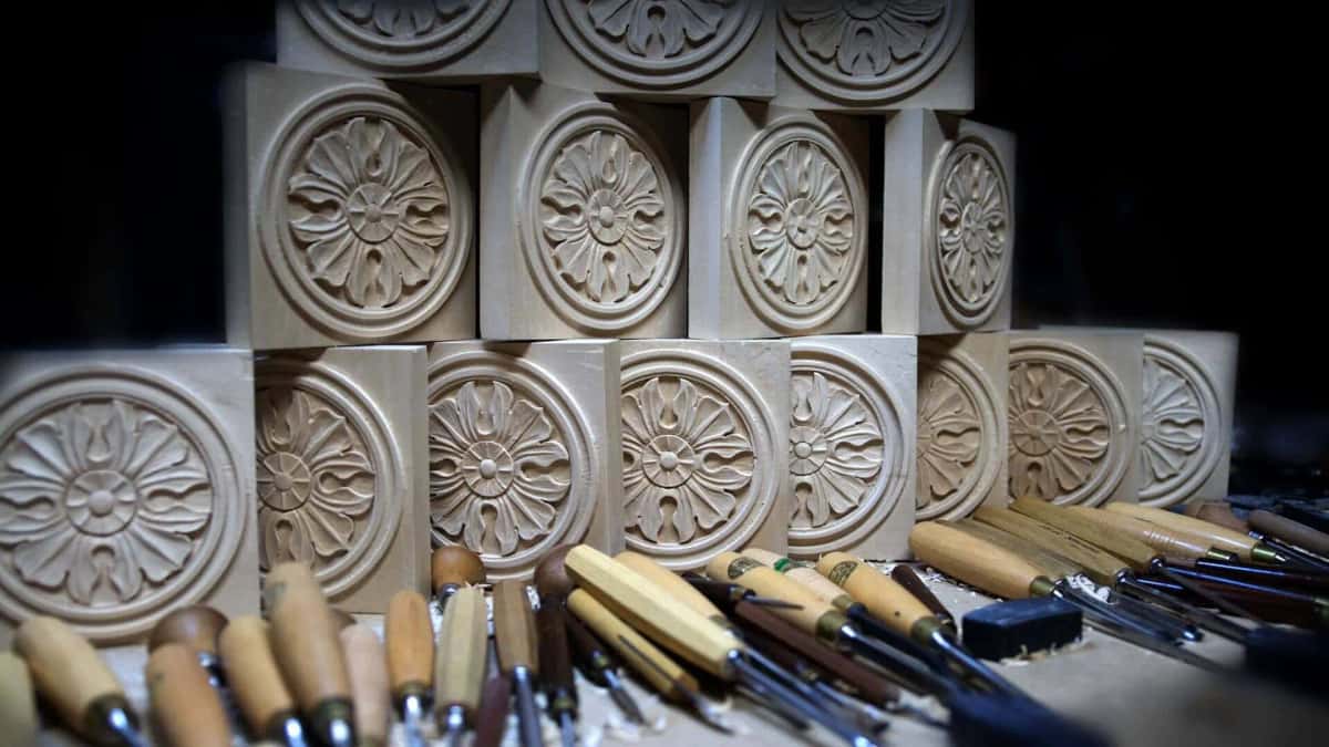 Fifteen carved basswood rosettes stacked in rows with carving tools in front