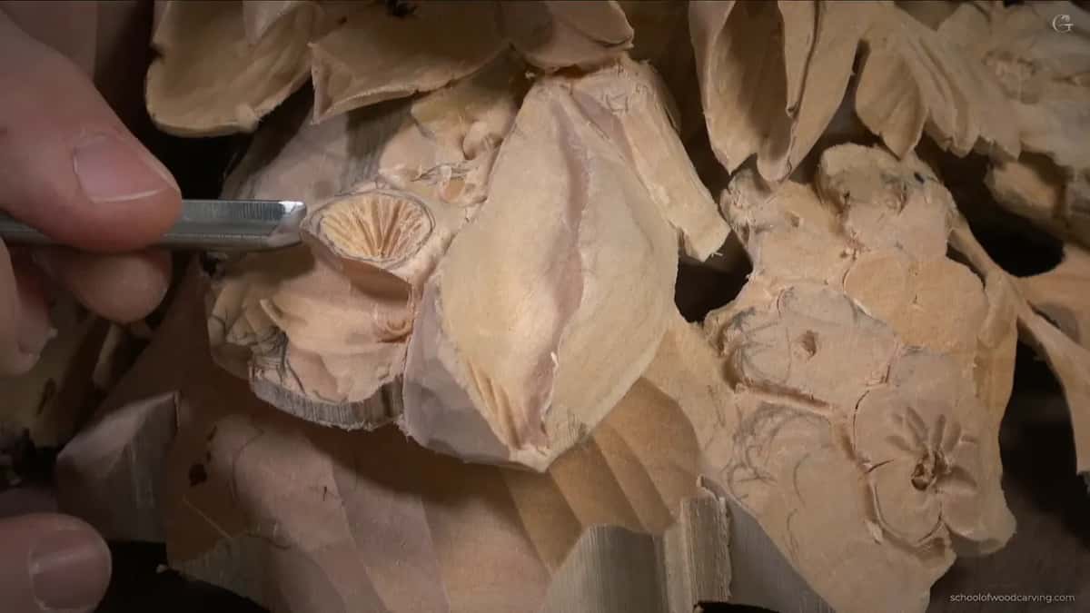 A blade held almost flat against a small carved rosette, whose sawn face shows the fibre ends fanning out in fine rays.