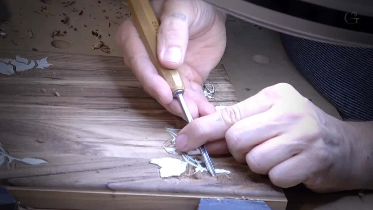 Two hands with a small gouge at the mitred corner of an olive box, where two runs of fibre meet each other at an angle.