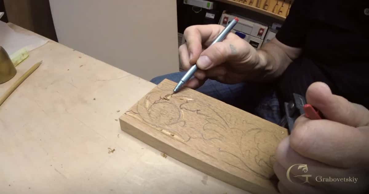 A pen traces a scroll on a small oak board.