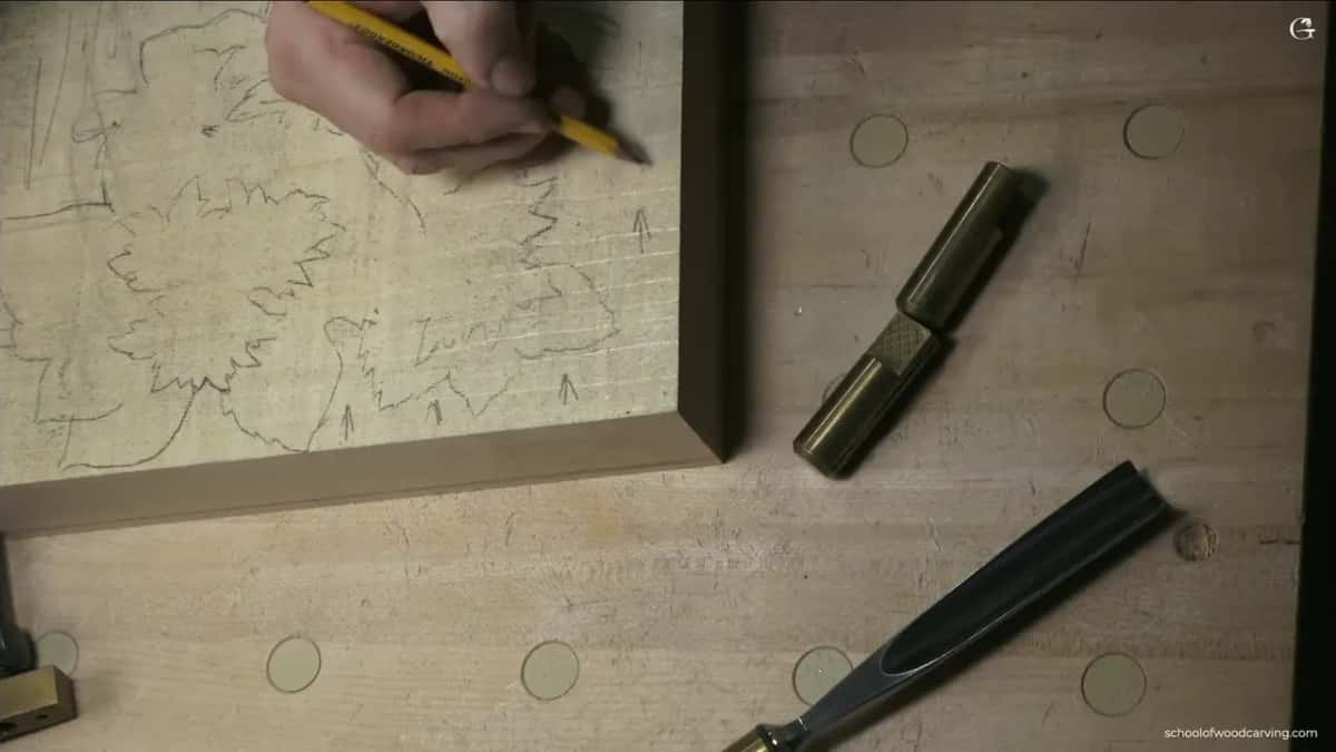 A hand draws pencil arrows on a blank to mark the direction of the grain before carving.