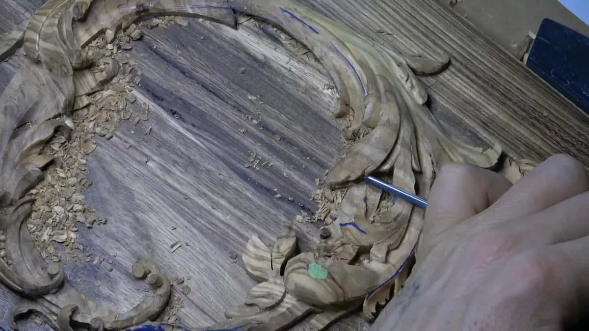 Deep ridges run across the sunken ground of an olive wood lid, blue marker lines around the scrolls.