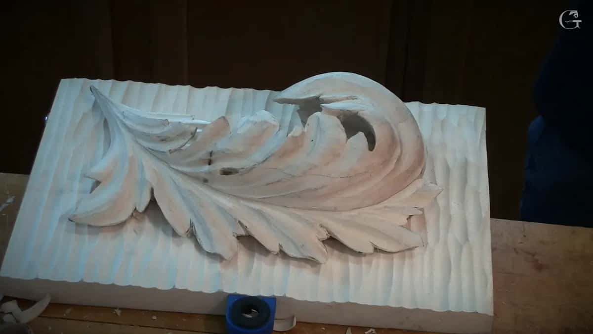 A finished acanthus leaf, smooth and pale, lying on a ground of deep parallel flutes that still carry every gouge stroke.