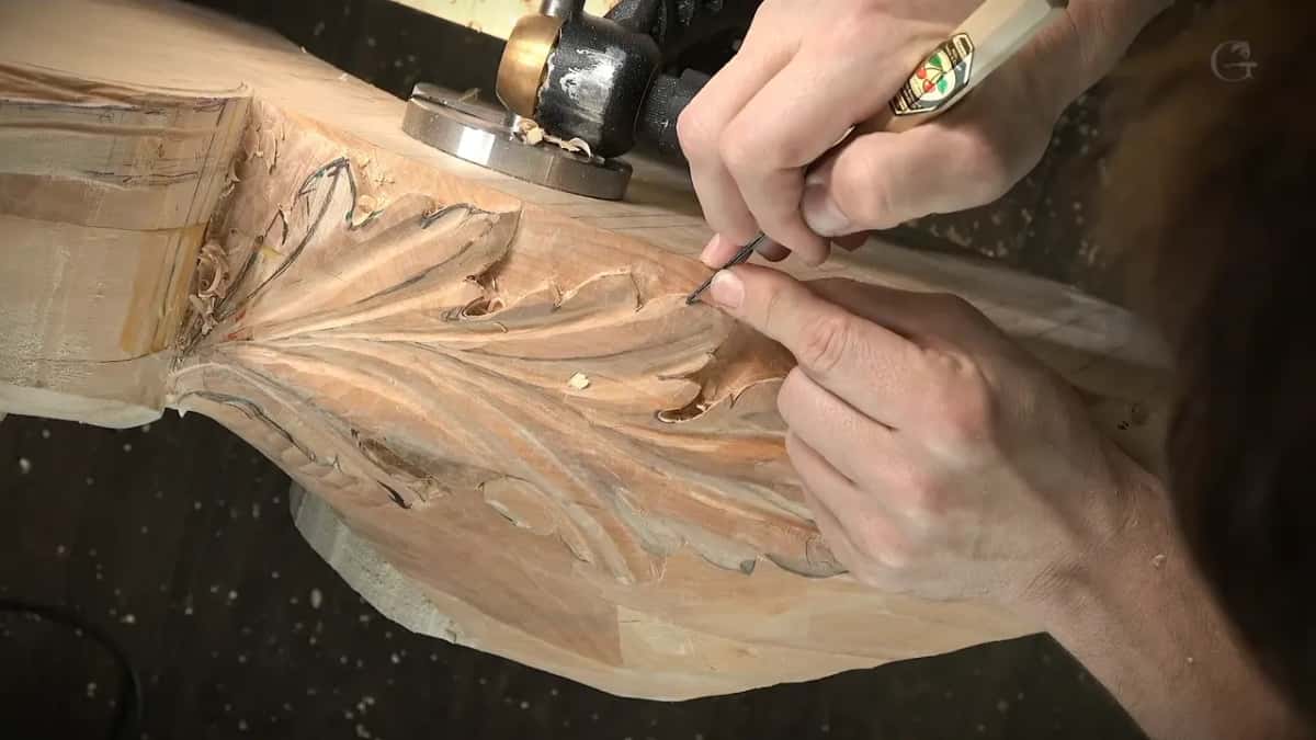 A V tool works the lobes of an acanthus leaf carved along a molding, chips gathered at one end.