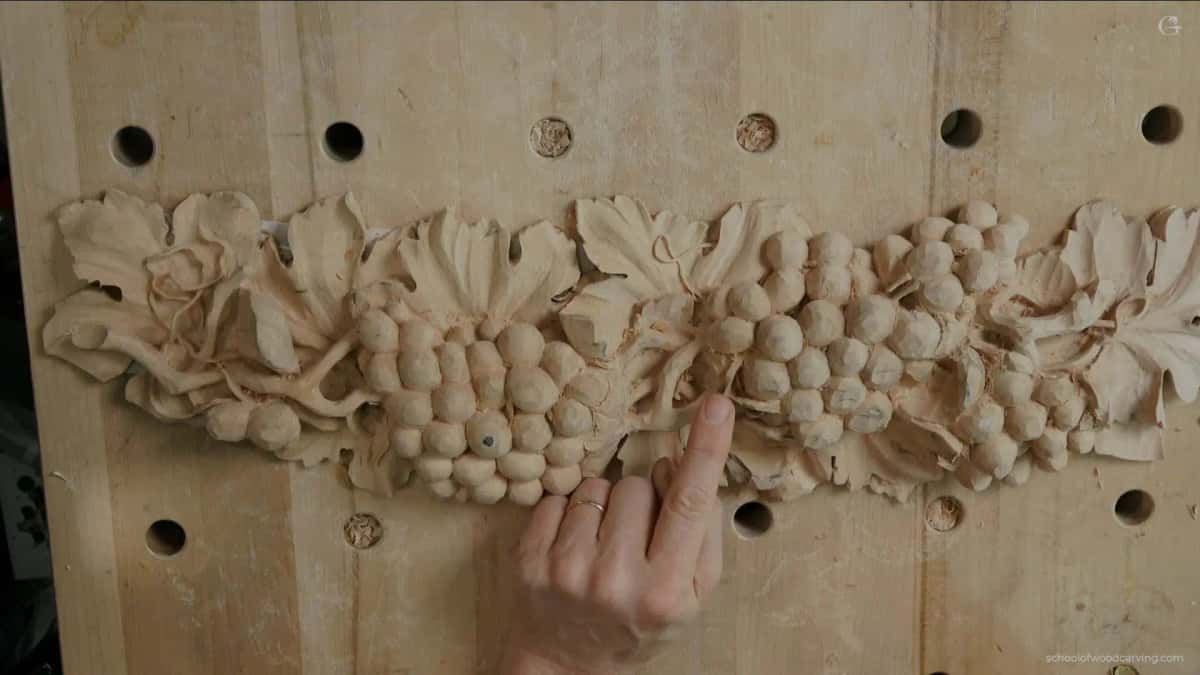 Grape bunches and leaves carved fully round with shadow beneath, a finger resting alongside for scale